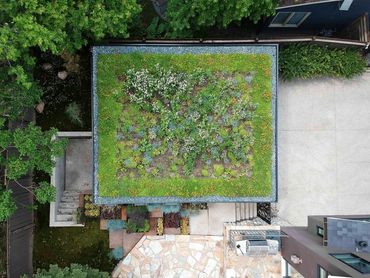 Aerial view of a building with a green roof surrounded by trees and a stone patio.