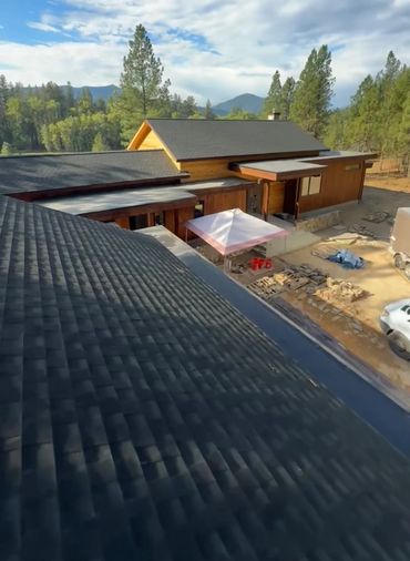 Modern wooden house under construction surrounded by trees and mountains.