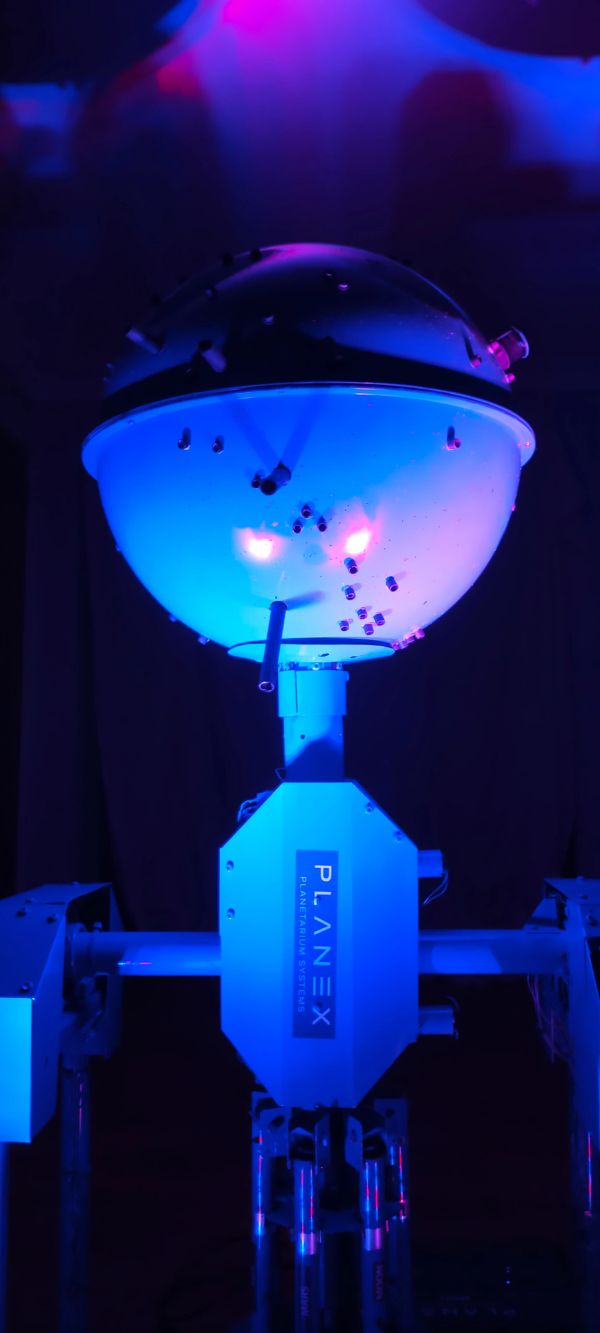A PLANEX planetarium projector illuminated in blue light.
