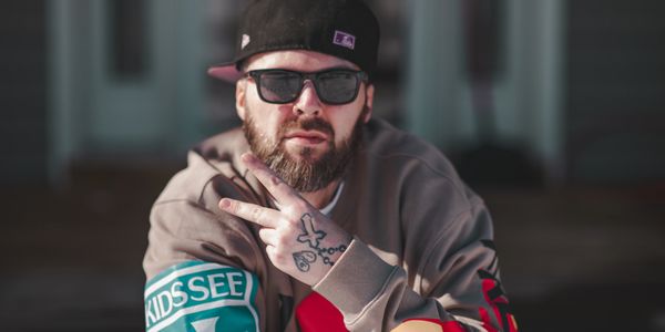 Man with beard, sunglasses, and cap shows peace sign with tattooed hand.