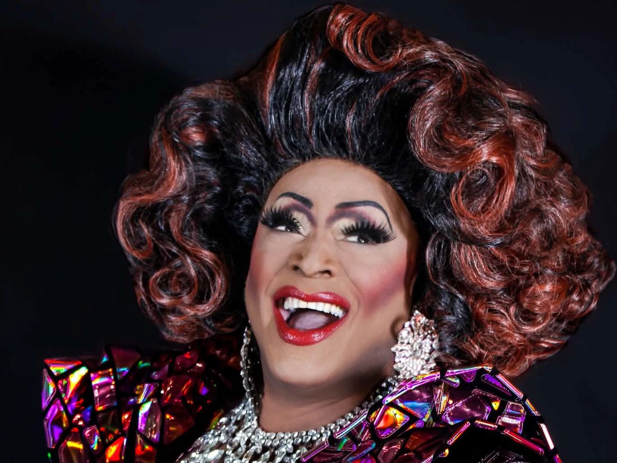 A person with vibrant makeup and colorful curly hair smiling.