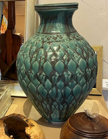 Large green ceramic vase with textured diamond pattern on a table.