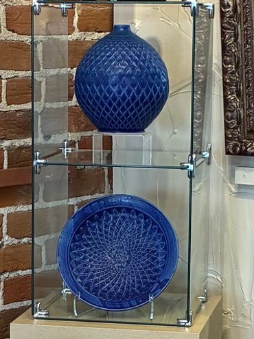 Two blue ceramic art pieces displayed in glass cases against a brick wall.