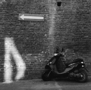 Black scooter parked against a brick wall with a left arrow sign.