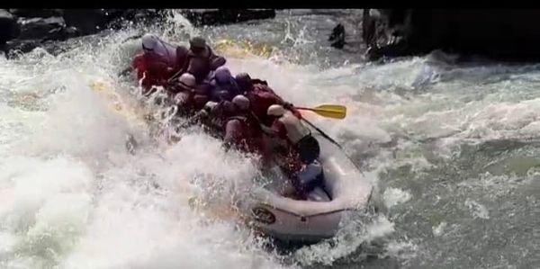 Group of people white water rafting through rapid river.