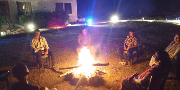 Group of people sitting around a campfire at night outdoors.