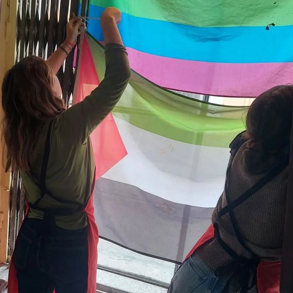 Dos personas cuelgan una bandera multicolor.