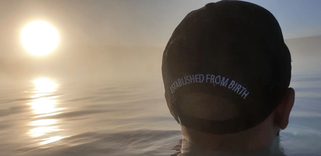 Model standing in lake wearing conSOULscious cap staring into the smoky sunset 