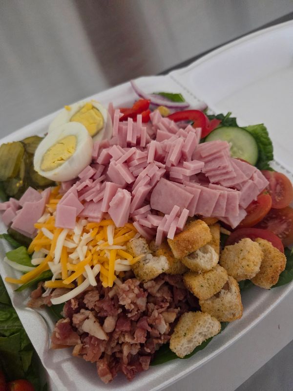 A colorful chef's salad with ham, cheese, egg, croutons, and veggies.