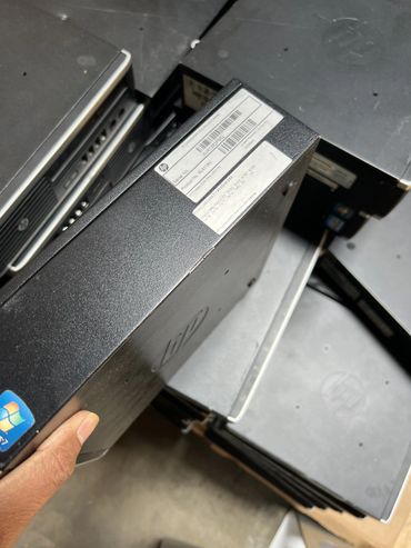 Hand holding an HP Compaq 8200 Elite PC with several similar units stacked.