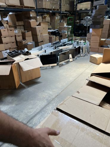 Warehouse filled with stacked cardboard boxes and rows of Apple iMac computers.