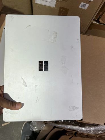 Hand holding a worn Microsoft Surface device with visible smudges and scratches.
