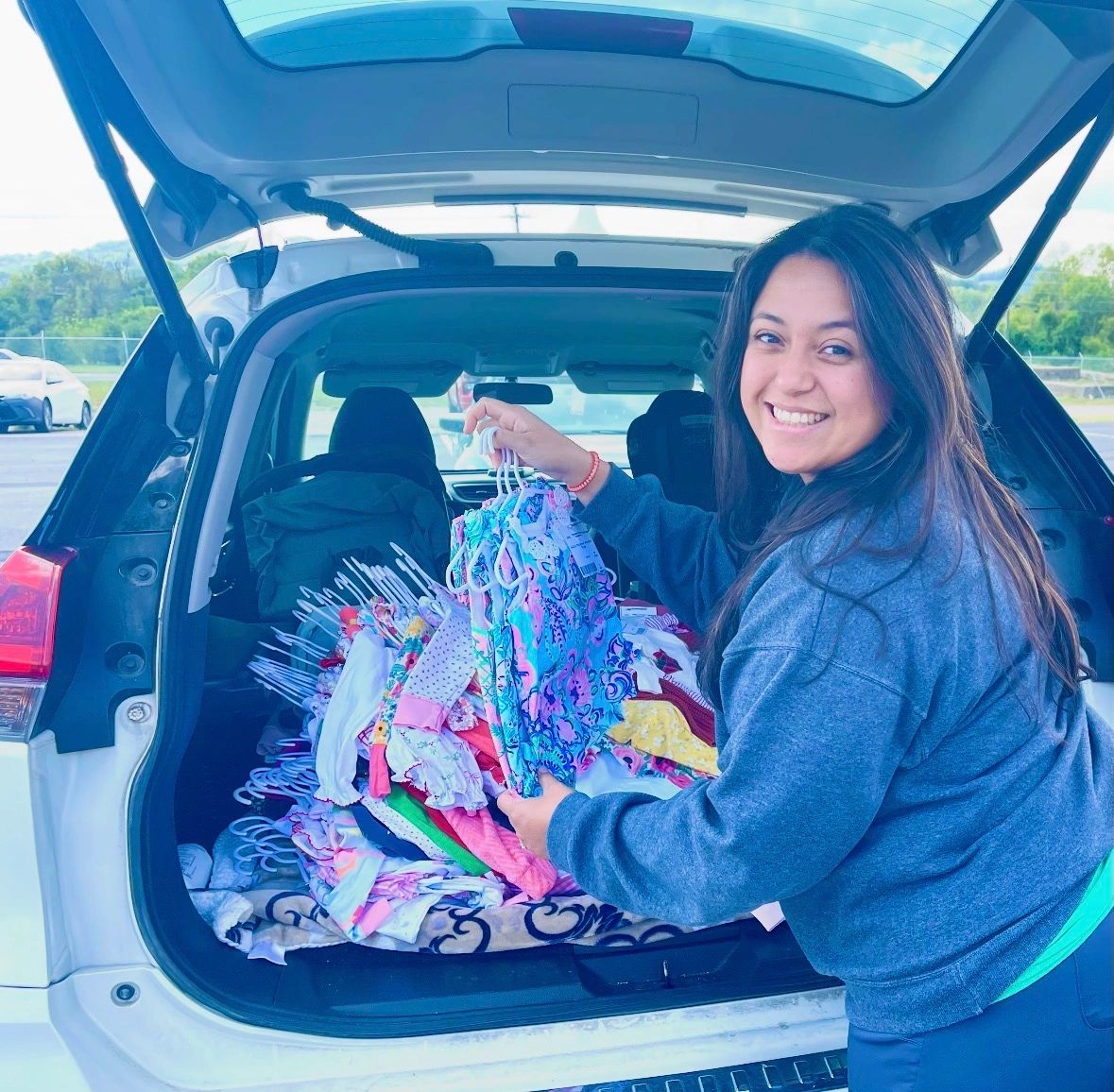 A woman smiling while organizing colorful clothes in the back of a car.