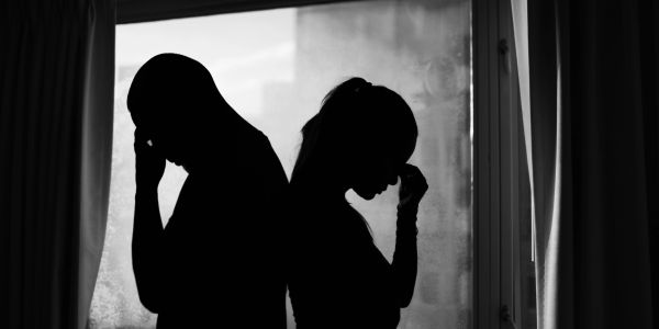 Silhouettes of a man and woman back to back, appearing upset.