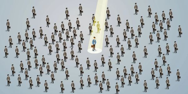 A unique businessman stands out in a crowd, highlighted by a spotlight.