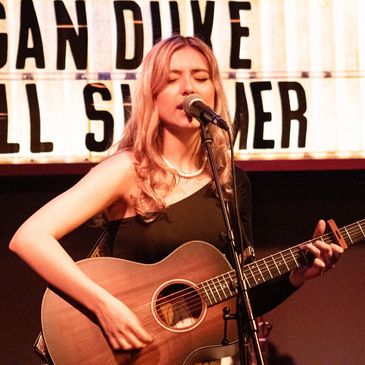 Julia Golden singing into a microphone while holding an accoustic guitar.