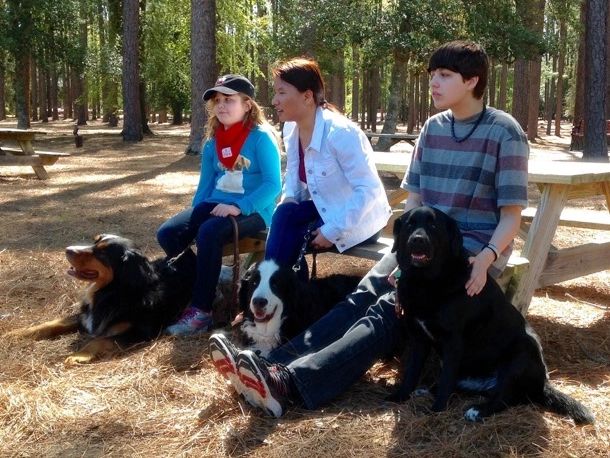 3 visually impaired children sitting in a forest with their guide dogs.