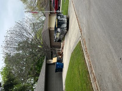 Residential driveway with a large dumpster and trash bins near a house.