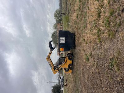 A yellow excavator loading debris into a black dumpster on a cloudy day.