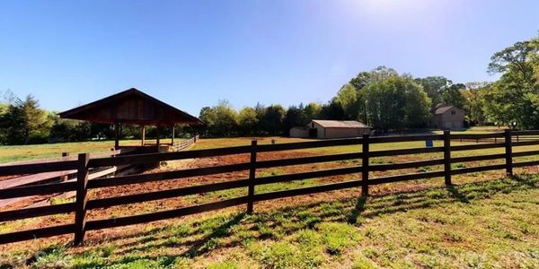 Sunny rural scene with wooden fence and farm buildings.