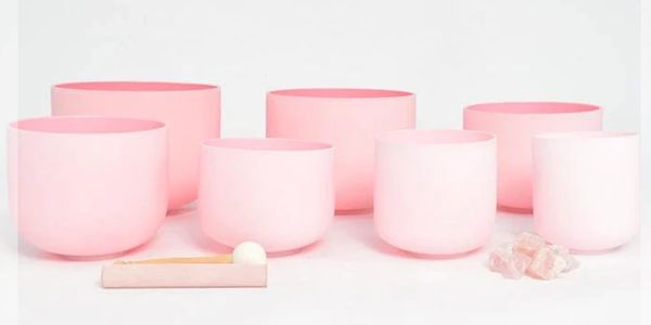 Set of seven pink singing bowls with a wooden mallet and rose quartz crystals.