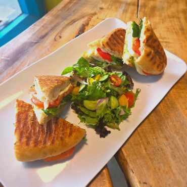 Grilled panini sandwiches with fresh salad on a white plate.