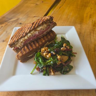 Grilled sandwich with melted cheese and meat, served with a fresh spinach salad.