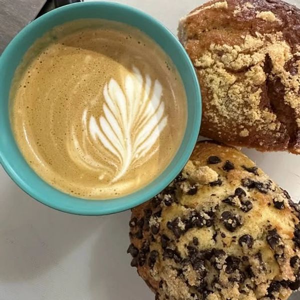 A cup of coffee with latte art and two muffins on a white surface.