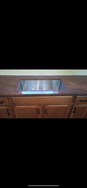 Stainless steel kitchen sink installed in a finished countertop with wood cabinets.