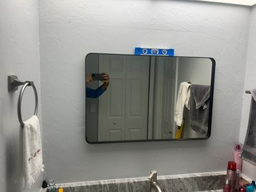 Installed wall mirror above a finished bathroom vanity and tile backsplash.
