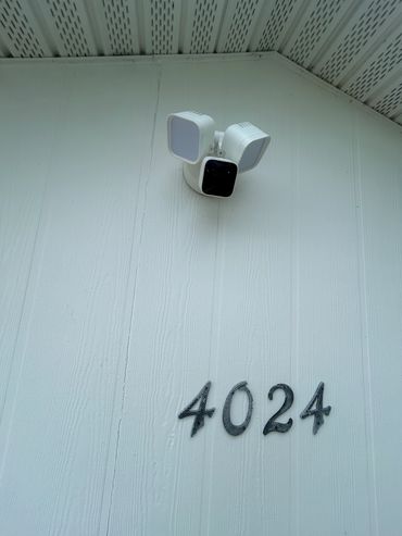 Exterior security camera and light installation above clearly mounted house numbers.