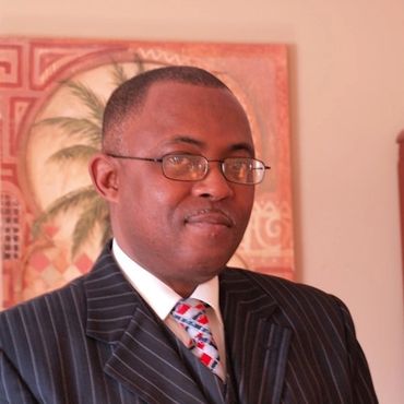 Man in a striped suit and glasses smiling indoors.