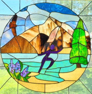 Stained glass depicting a person surfing near a mountain and tree.