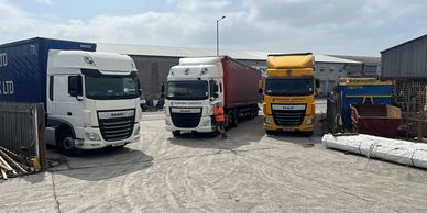 Four trucks parked outside an industrial warehouse on a cloudy day.