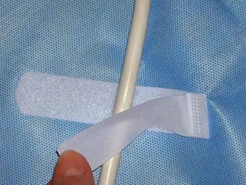 A hand holding a white cable secured by a Velcro strap on blue fabric.