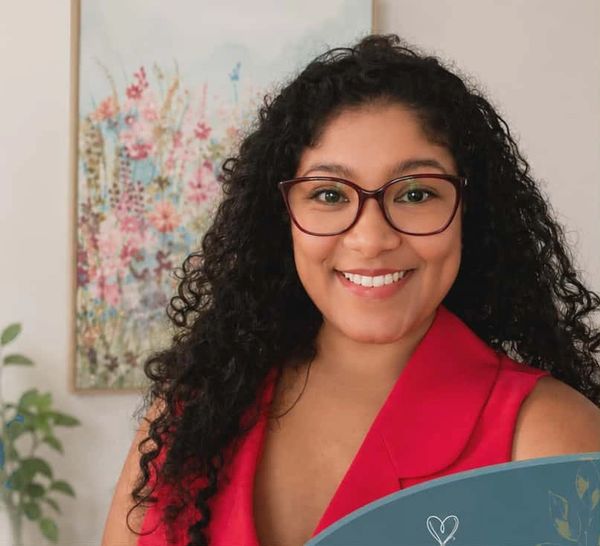 Smiling woman with curly hair and glasses in a red top.