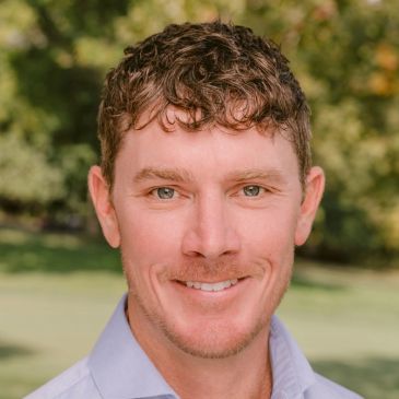 Smiling man outdoors with curly hair.