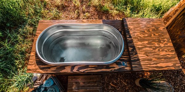 Handcrafted Tundra Tub Cold Therapy Tub placed alongside a river in an outdoor spa setting.