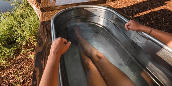Woman relaxing in a handcrafted Tundra Tub Cold Therapy plunge placed alongside a river.