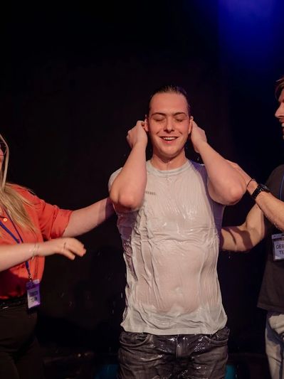 Man in wet white shirt smiling with friends on stage.
