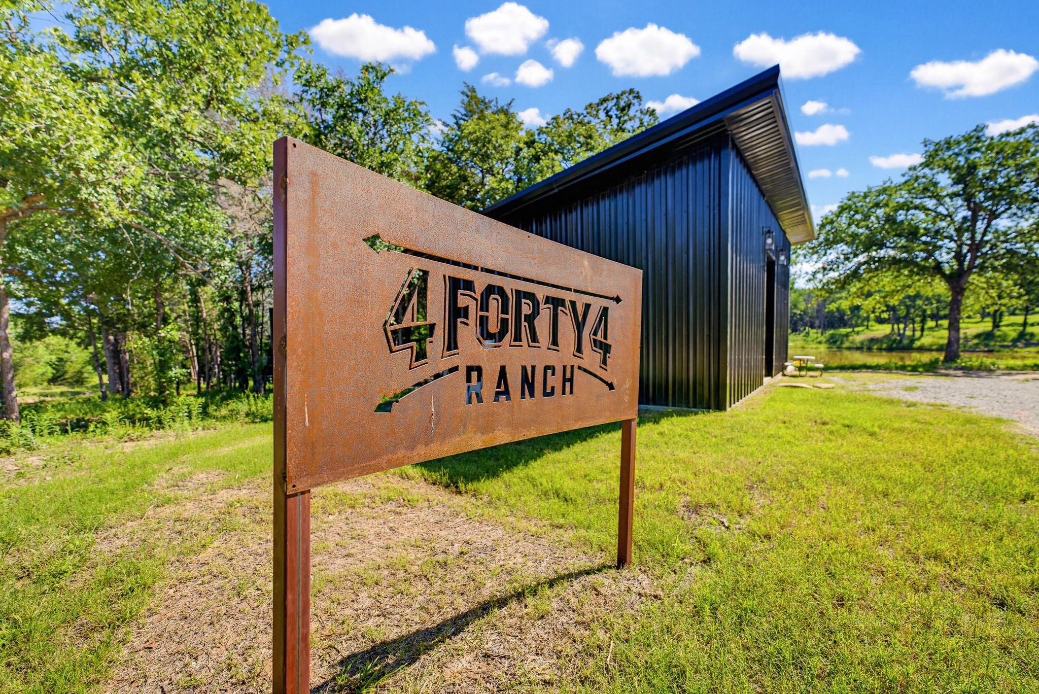 Rustic sign for 4Forty4 Ranch with black barn and green landscape.