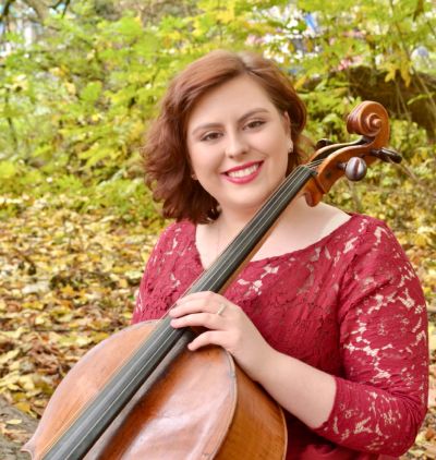 Woman smiling with cello outdoors.