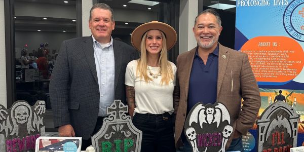 Three people smiling behind Halloween-themed tombstone decorations at an event.