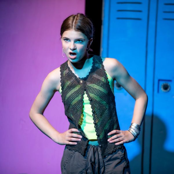 A young woman performs confidently on stage with dramatic lighting.