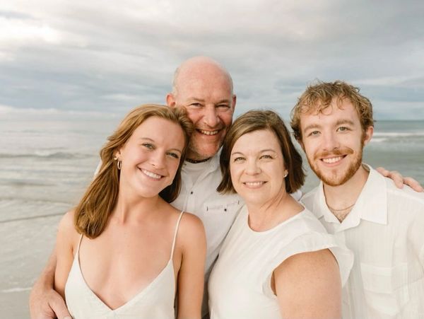 A happy family of four posing together on a beach.