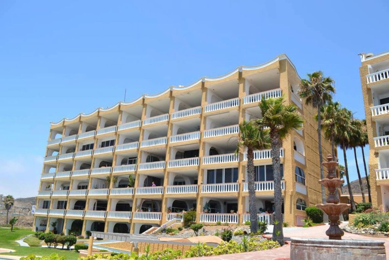 Large beige apartment building with balconies and palm trees.