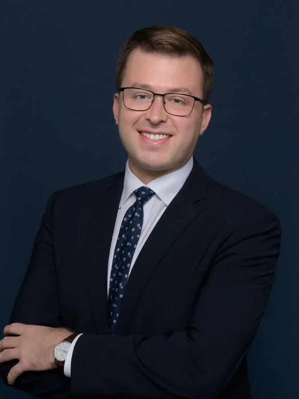 Professional young man in suit and glasses smiling confidently.