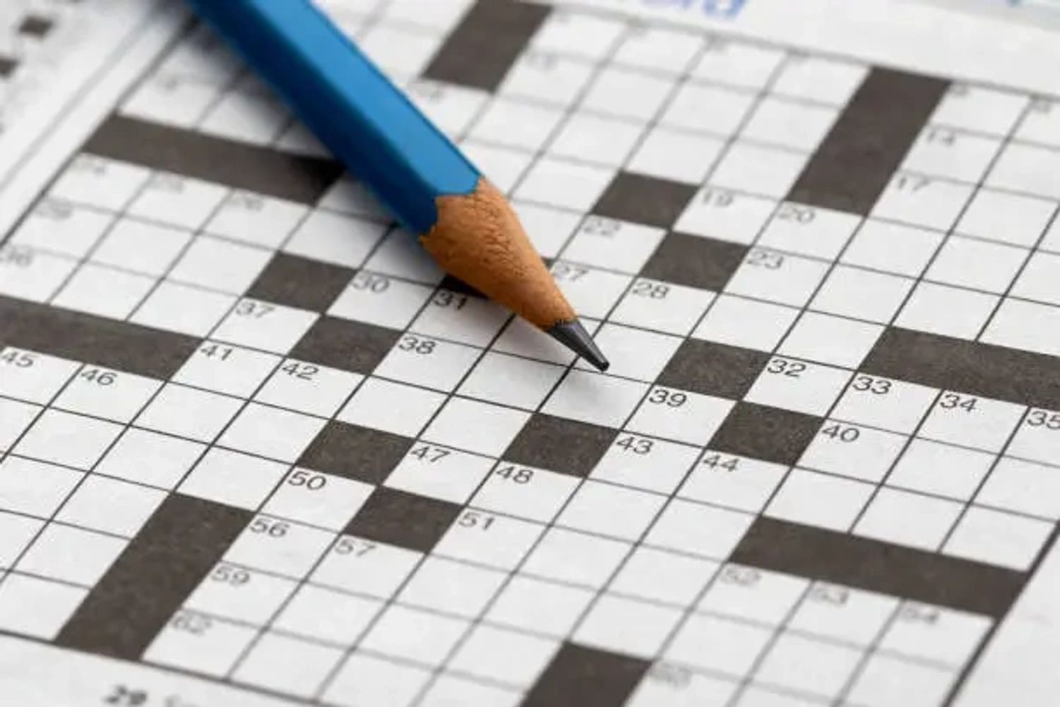 A blue pencil resting on a crossword puzzle.