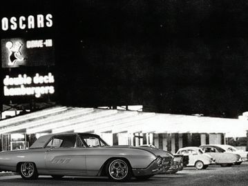 Black-and-white photo of vintage cars parked near a diner at night.