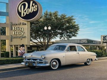 Vintage car parked outside Bob's Big Boy restaurant with clear blue sky.